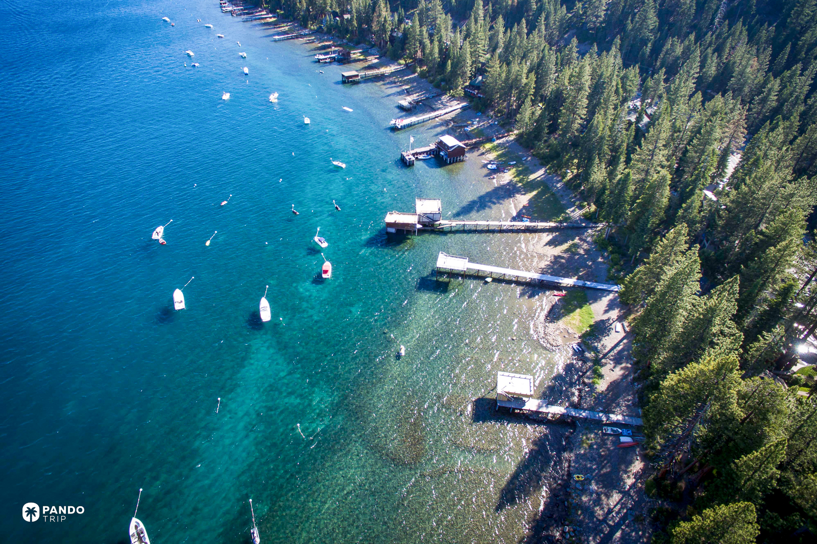 Piers, moored boats and a stony bottom visible through the shallows of Lake Tahoe from the air.