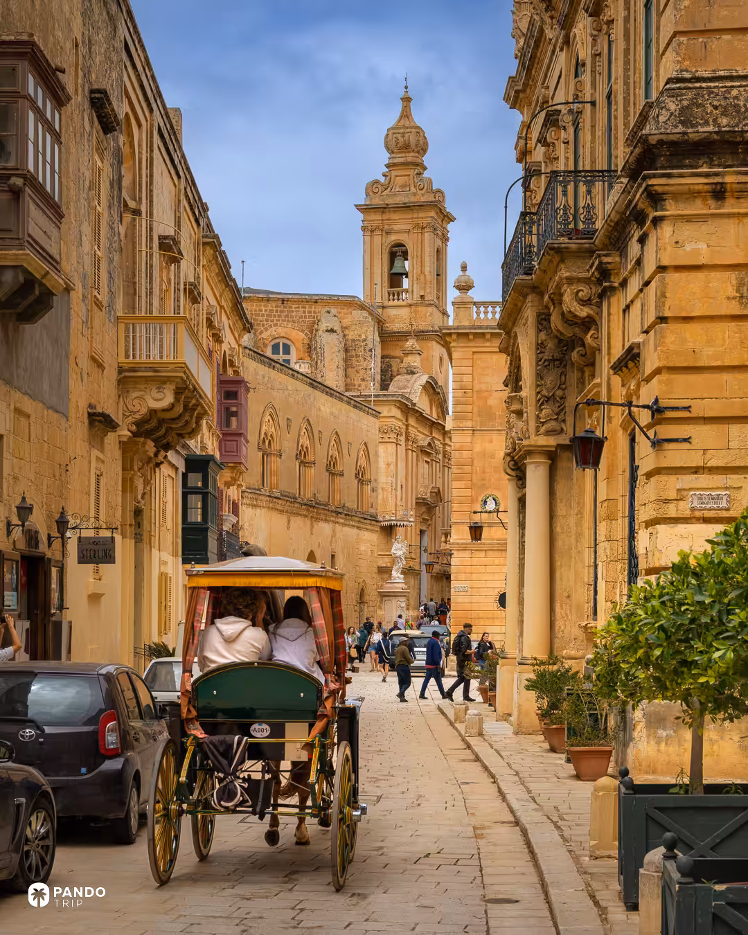 A karrozzin horse cab waiting on a limestone lane in Mdina, a church tower rising behind the rooftops.