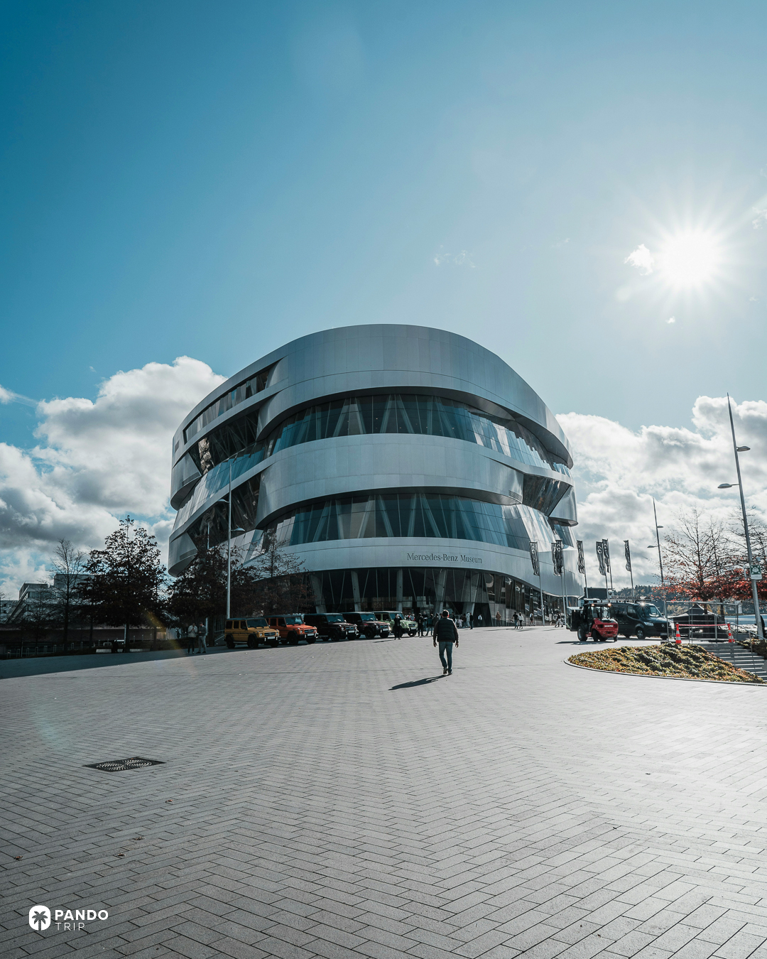 The silver drum of the Mercedes-Benz Museum in Stuttgart seen across its empty forecourt in low sun.