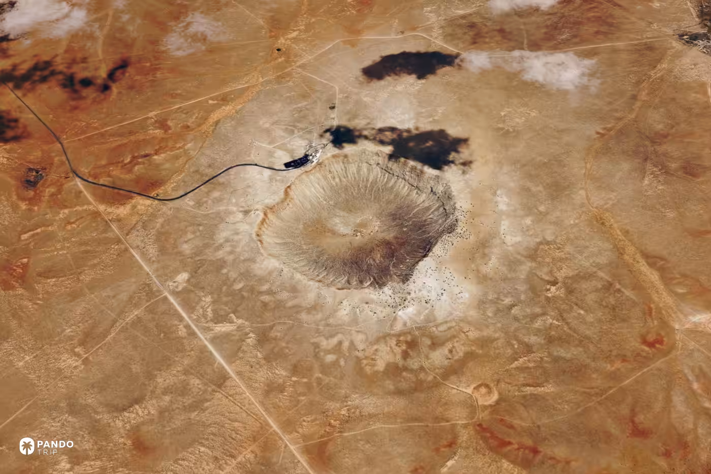 Satellite view of Barringer Crater in the Arizona desert, a pale bowl with a single road running to its rim.