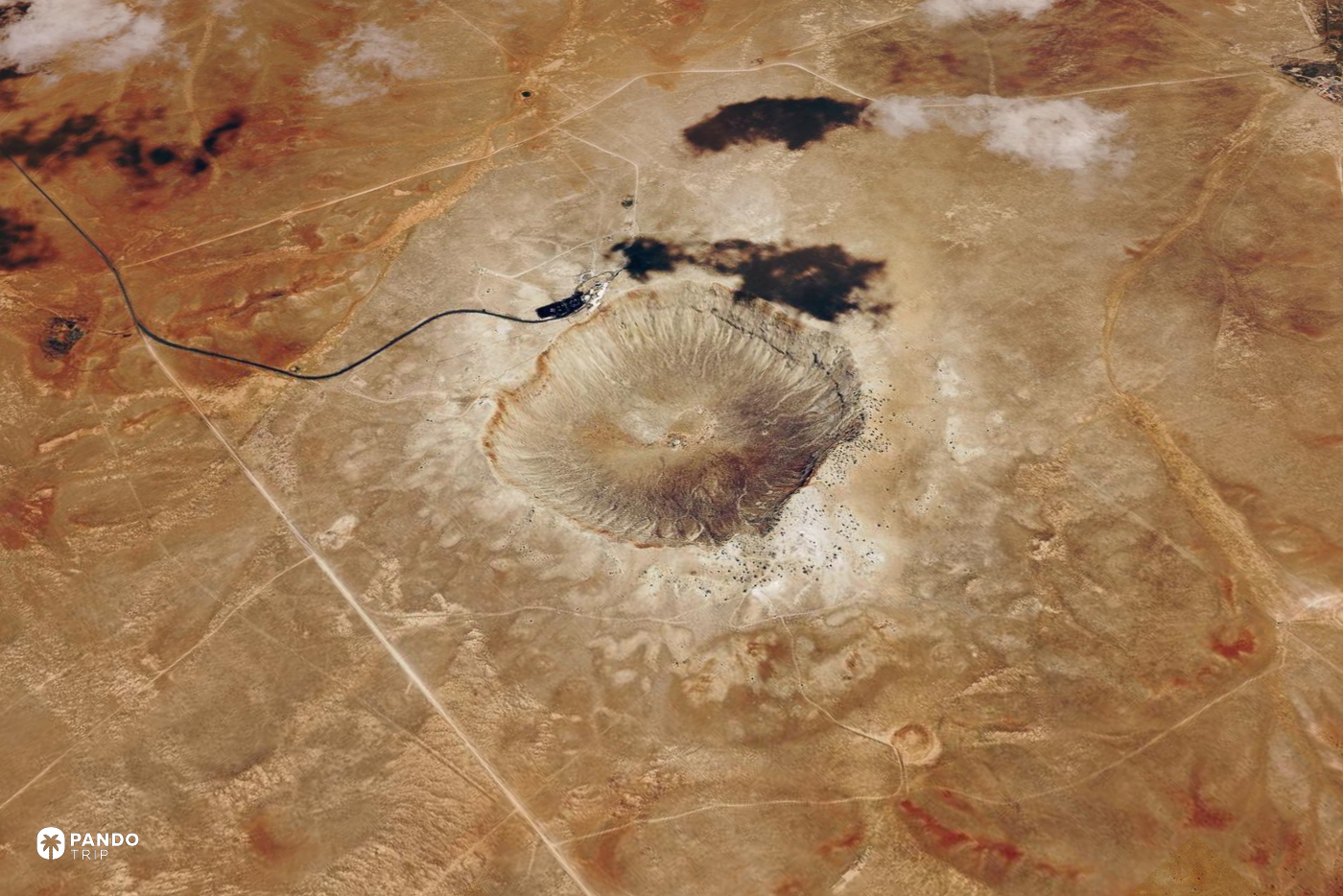 Satellite view of Barringer Crater in the Arizona desert, a pale bowl with a single road running to its rim.