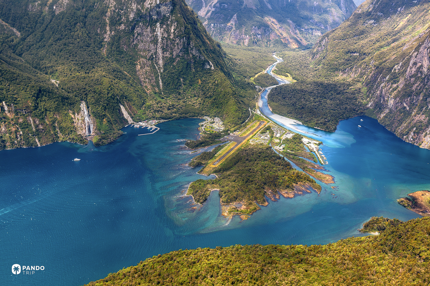 The head of Milford Sound from above, the airstrip and terminal filling the flat land between the mountains.