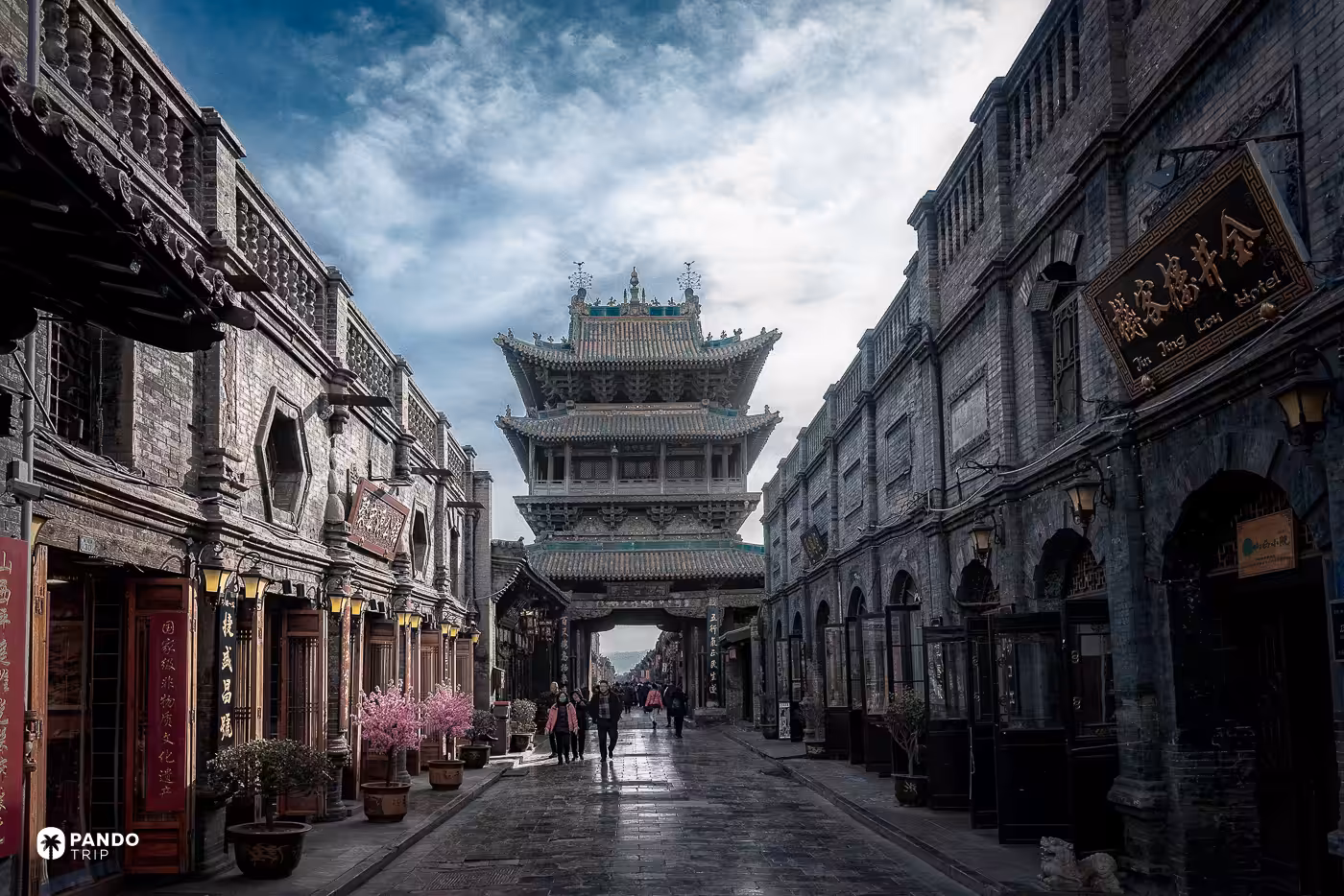 Grey-brick shopfronts along a street inside Pingyao's walls, the tiered city tower rising at the end of it.