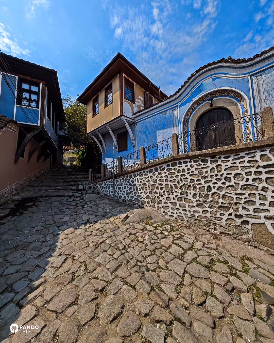 A blue-painted National Revival house with an ornate arched oriel window on a cobbled lane in Plovdiv's old town.