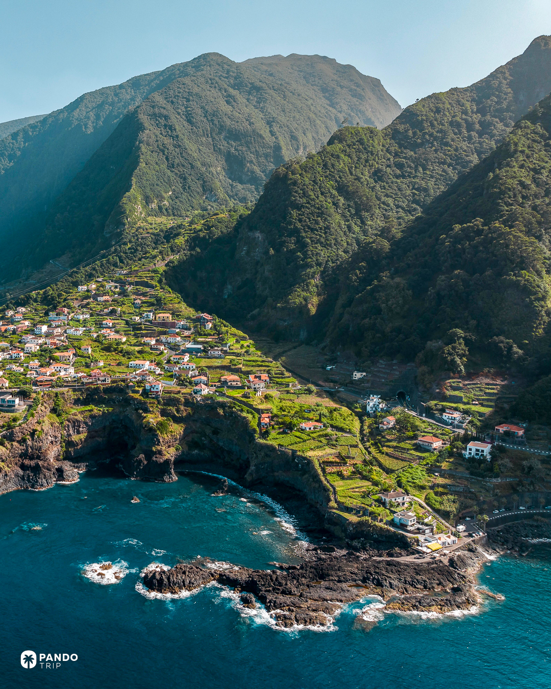 Terraced houses on green cliffs above black volcanic rock and turquoise water at Seixal, on Madeira's north coast.