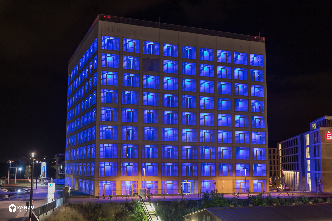 Stuttgart City Library glowing blue at night, its glass-block grid lit and LIBRARY lettering on the concrete.