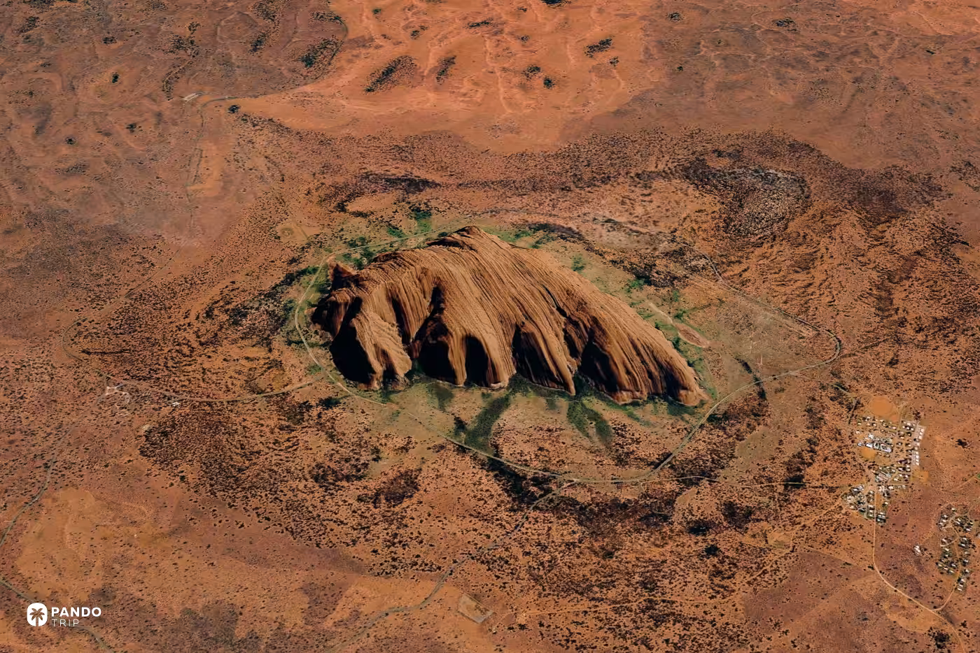 Satellite view of Uluru rising from red desert, encircled by the national park's loop road.