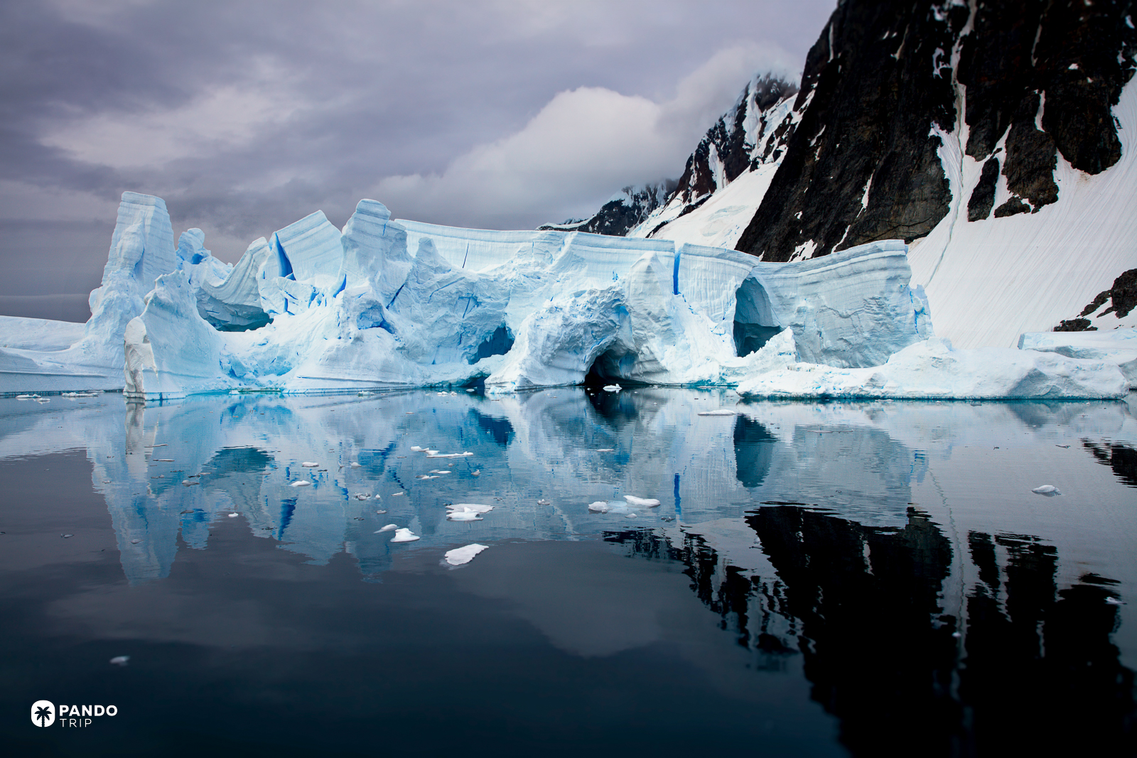 Blue ice cliffs and their reflection in still dark water off Antarctica.
