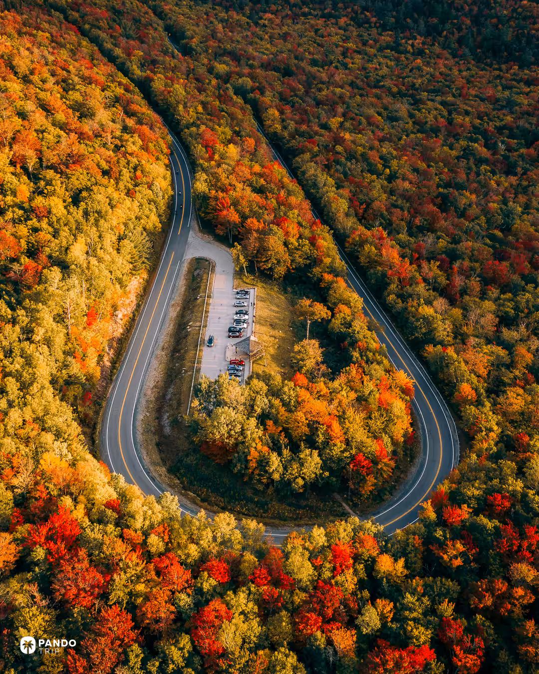 Aerial view of the hairpin bend at Hancock Overlook on the Kancamagus Highway, with a parking area inside the loop and red and yellow forest around it.