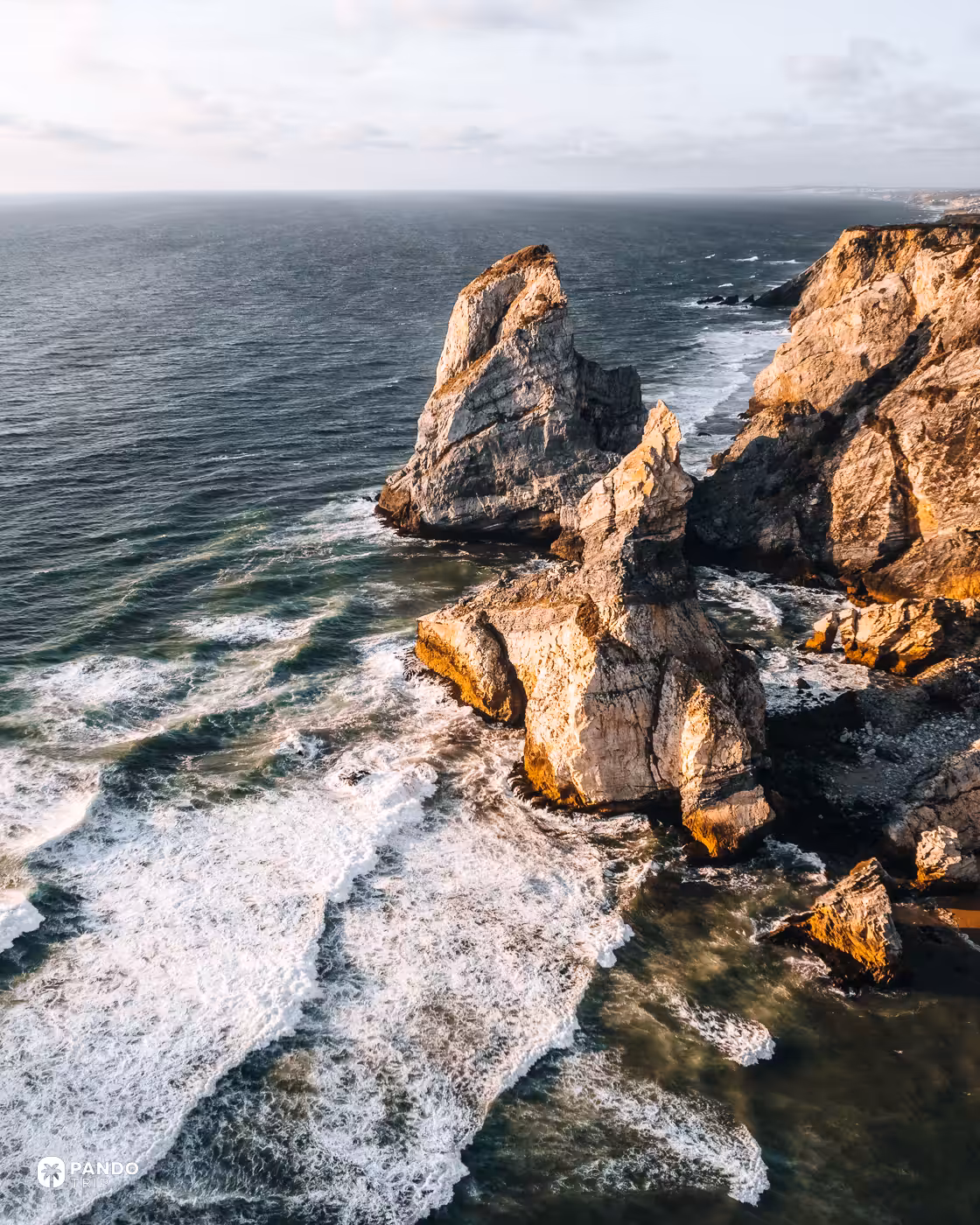 The two sea stacks of Praia da Ursa in evening light with Atlantic surf around them