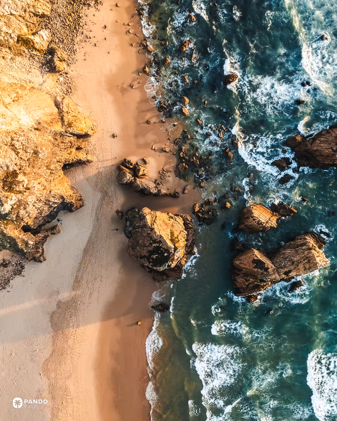 Top-down view of sand, boulders and surf at Praia da Ursa