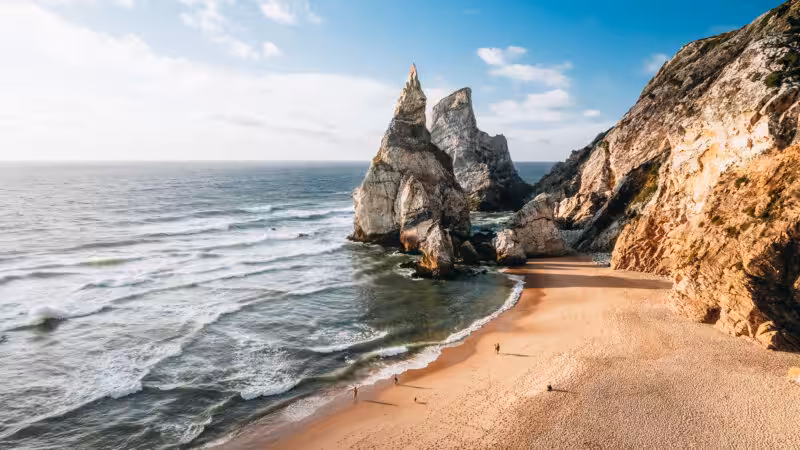 Two limestone sea stacks rising beside the sandy beach at Praia da Ursa, Sintra, Portugal