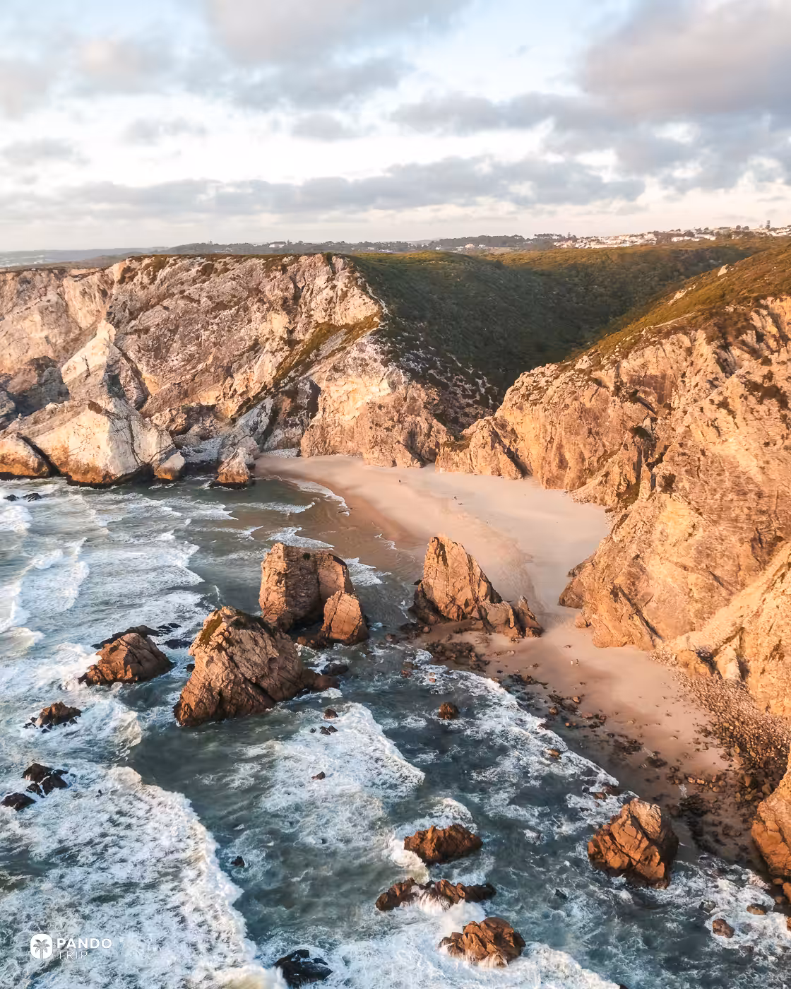 Praia da Ursa cove and the green valley behind it, with the village of Azóia on the ridge