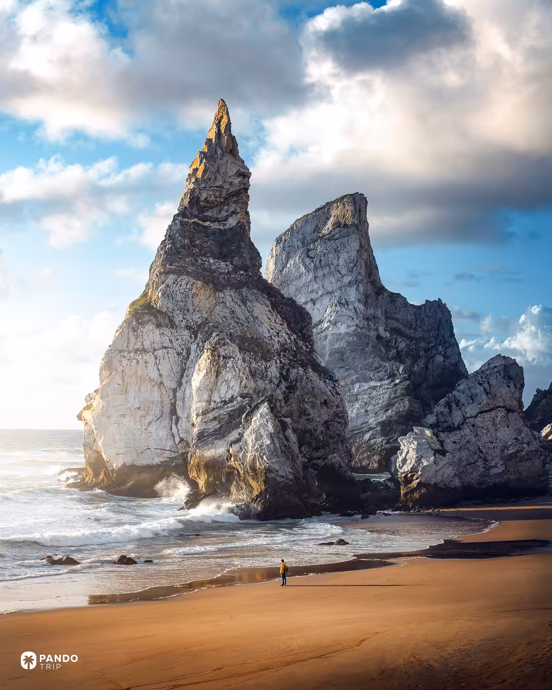A lone walker on the sand beneath the pointed limestone stack at Praia da Ursa