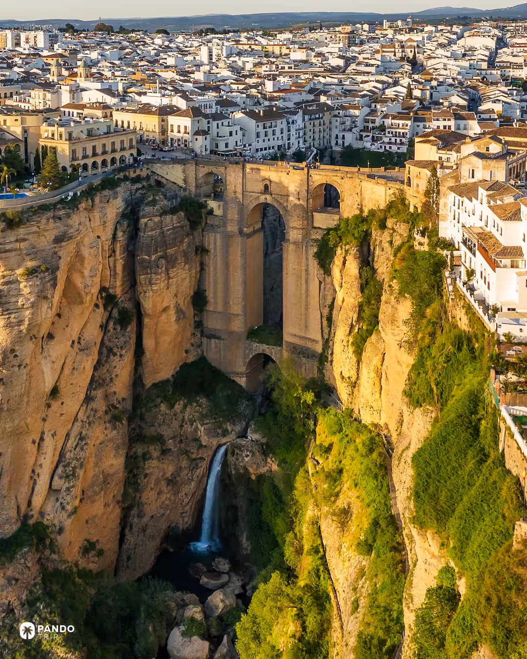 The Puente Nuevo bridging the El Tajo gorge in Ronda, whitewashed houses lining the cliff top and a waterfall at the base.