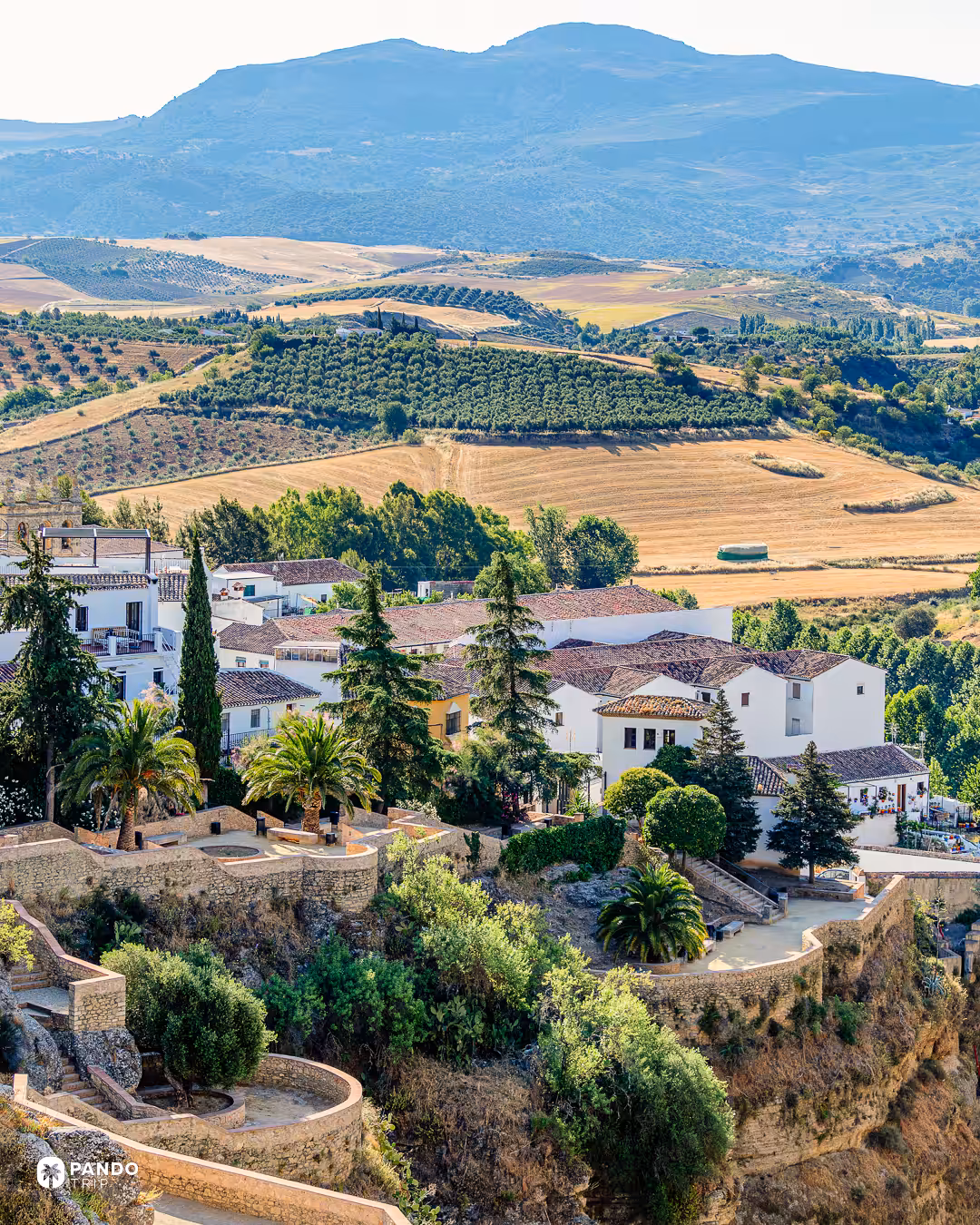 Terraced gardens and white houses on the edge of Ronda, overlooking olive groves, fields and mountains.