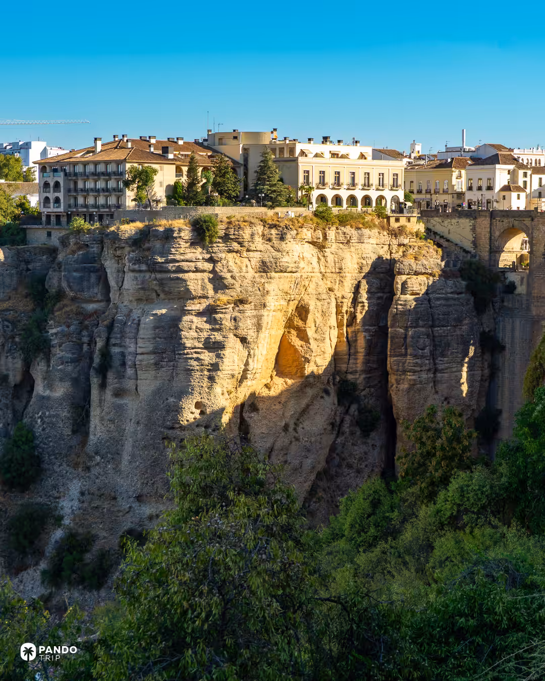 Buildings on top of Ronda's ochre cliffs, with the Puente Nuevo at the edge of the frame.