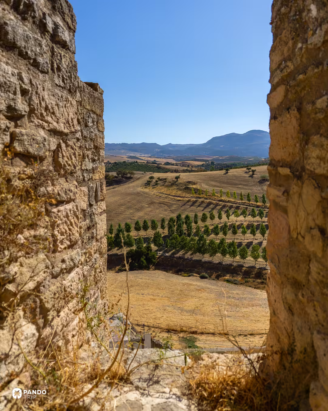 Farmland and mountains outside Ronda seen through a gap in old stone walls.