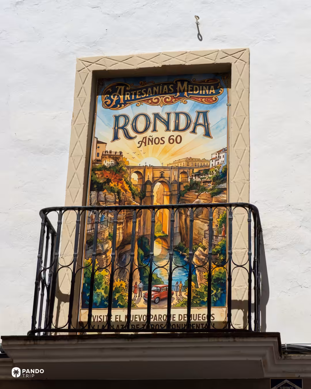 A painted tile poster reading 'Ronda Años 60' on a whitewashed wall above an iron balcony.