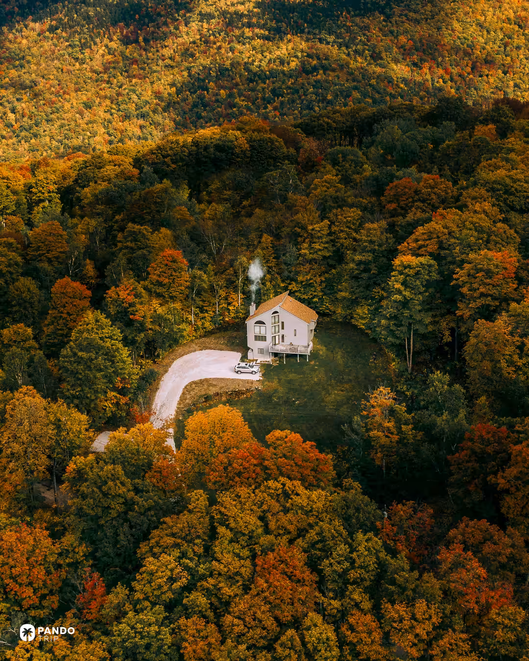 Aerial view of a house with smoke rising from its chimney in a clearing in autumn forest in Vermont.